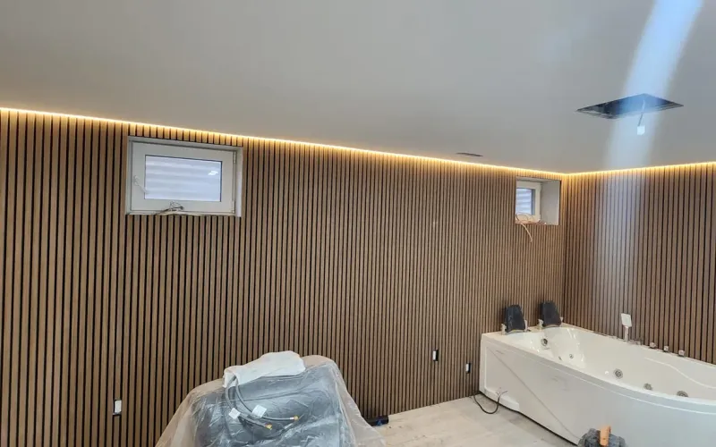 Finished lower-level room in a GTA home with wood slat walls, small high windows and cove lighting, before final fixtures are set
