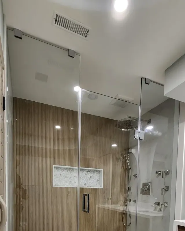Walk-in glass shower with wood-look ribbed wall tile, a long marble niche and a rain head, a small rectangular grille in the ceiling inside the glass and a larger grille in the ceiling outside it