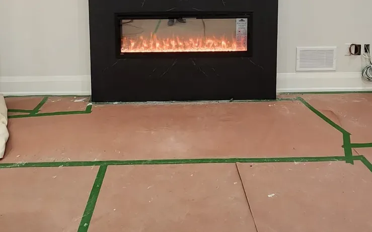 Black stone fireplace wall with the fire lit, and the floor in front of it covered with sheets of protection board joined with green tape