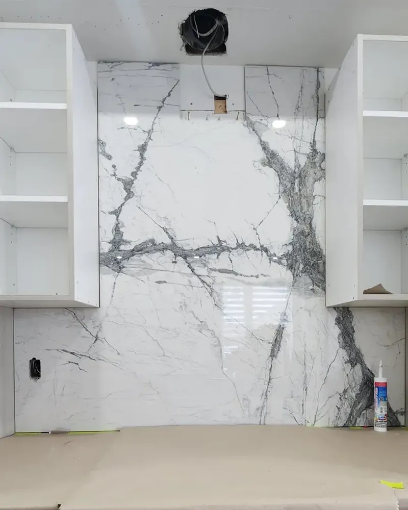 Two white upper cabinet boxes with adjustable shelves and no doors, hung either side of a veined white slab backsplash below an open hood duct