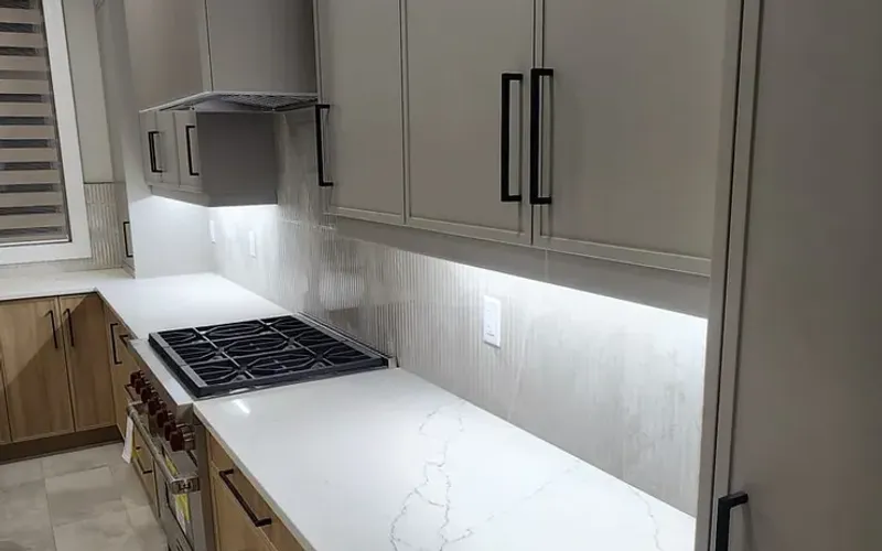 Kitchen with greige shaker upper cabinets and long black pulls, a white quartz counter, a gas cooktop and oak-look lower drawers under LED strip lighting