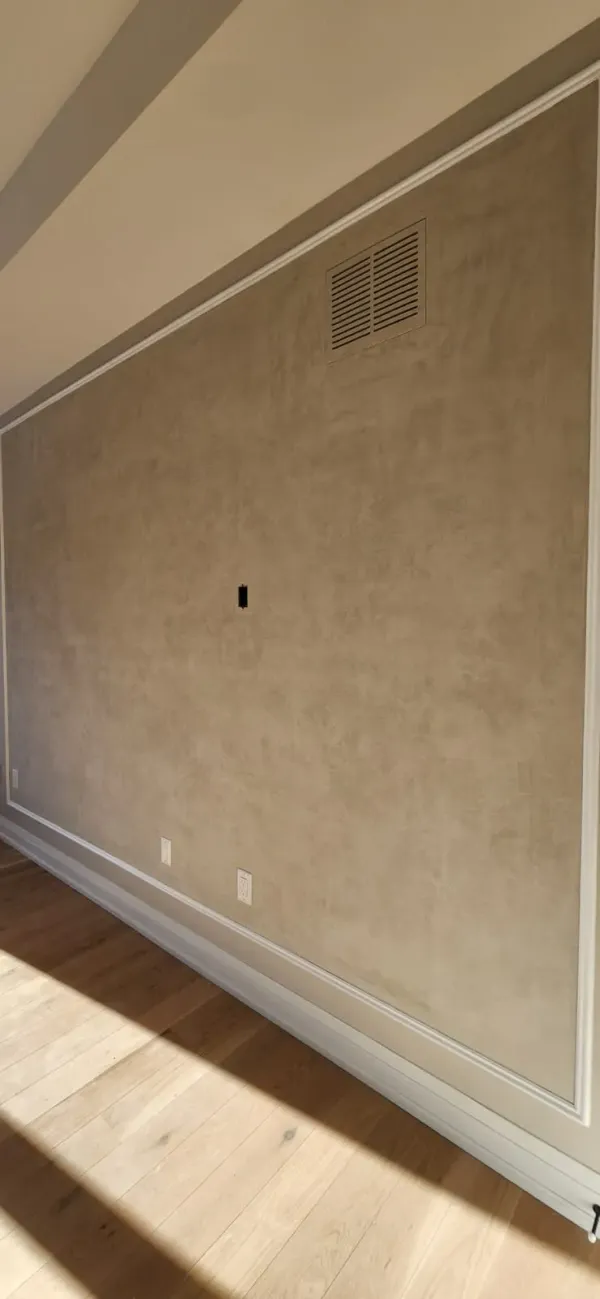 Beige troweled plaster panel framed in white moulding, with a cable opening at mid height, two outlets low on the wall and a return-air grille near the ceiling