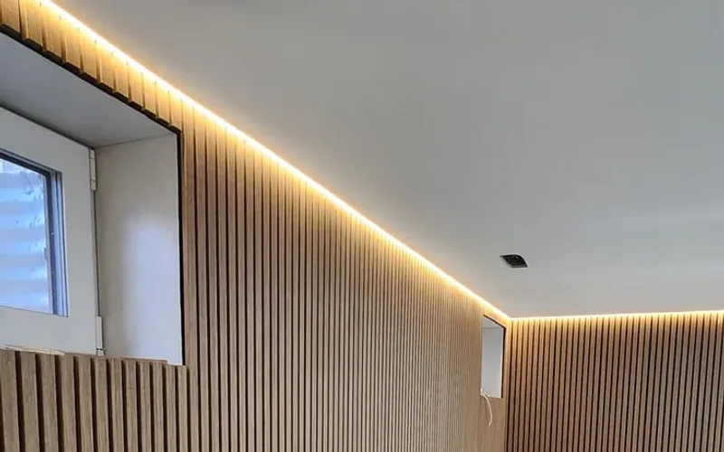 Dining room under renovation with recessed ceiling lights, a glowing LED strip along the ceiling edge, a rectangular chandelier and herringbone wood floor partly covered with protective board