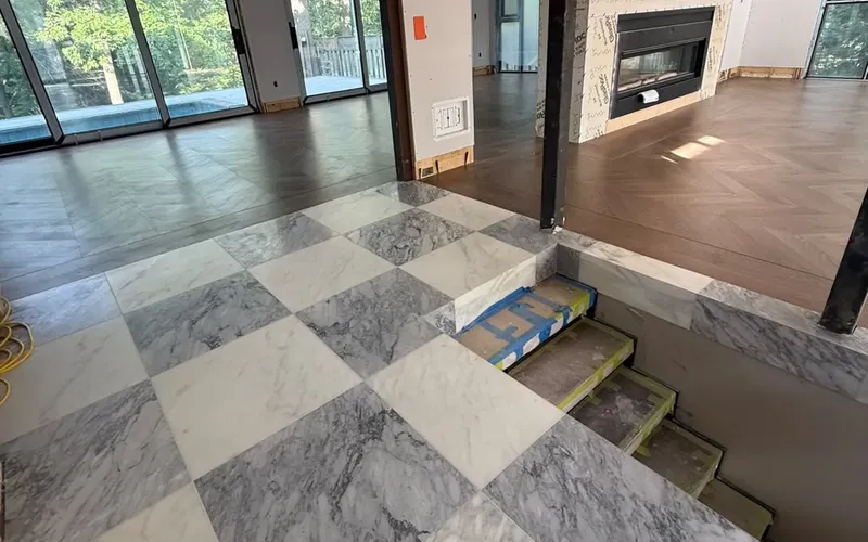 Grey and white stone tile landing meeting herringbone wood flooring in an open-plan GTA home during renovation