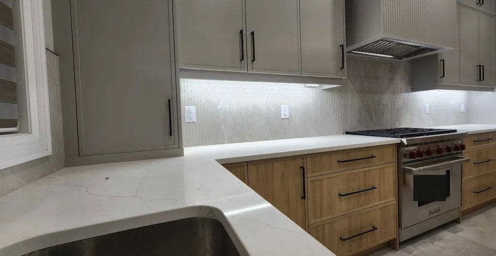 Kitchen with grey upper cabinets, ribbed porcelain backsplash, quartz counters, a range under a fluted hood and a window at the left