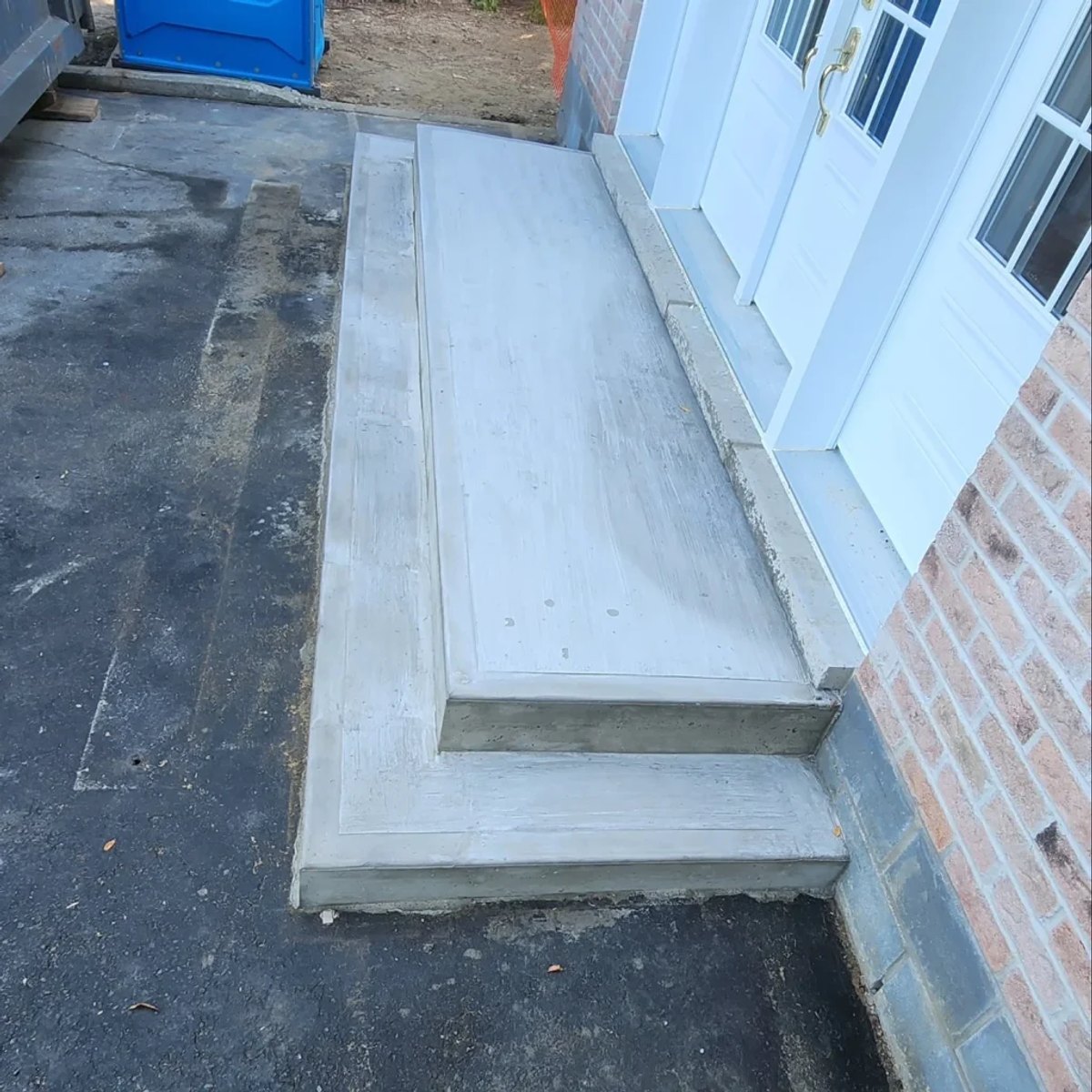Two-step concrete landing in front of a white double door beside a brick wall