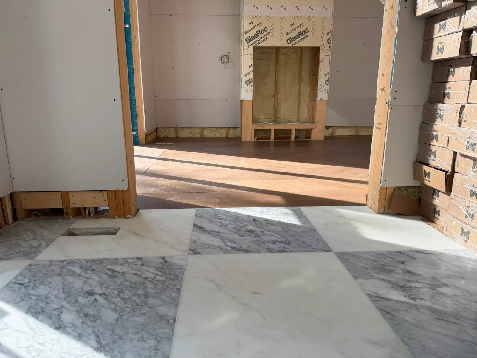 Marble floor in the hall, oak in the next room, and a fireplace opening still showing framing and spray foam insulation