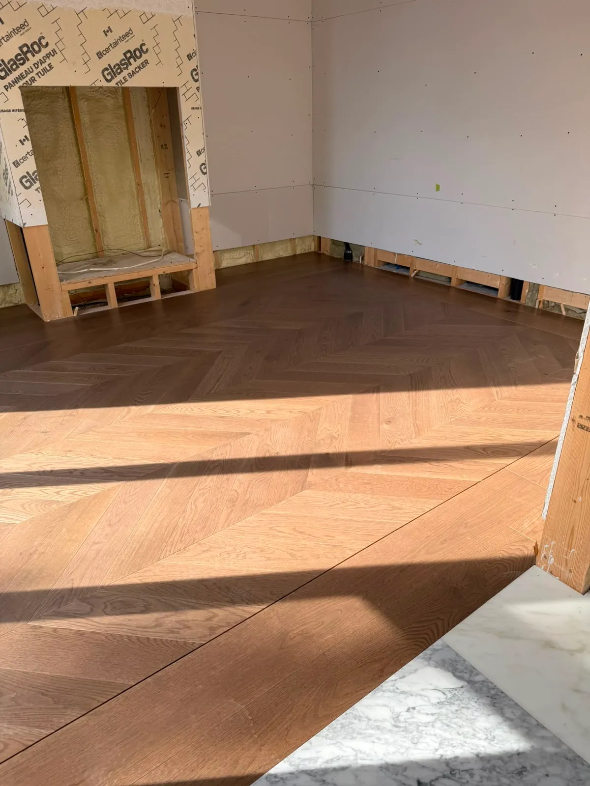 Room with walls boarded and chevron oak floor laid; a framed niche lined with GlasRoc tile backer still shows the insulation inside