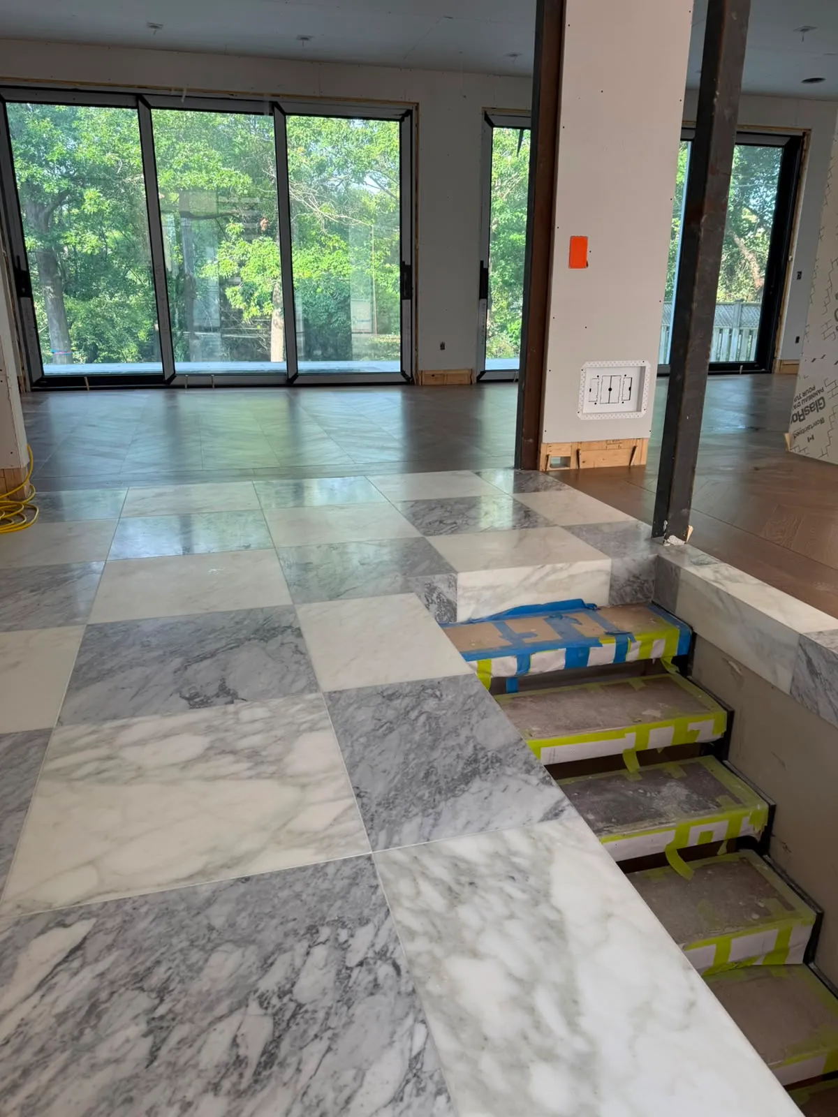 Grey and white marble squares meeting oak flooring, with stair treads wrapped in protective tape