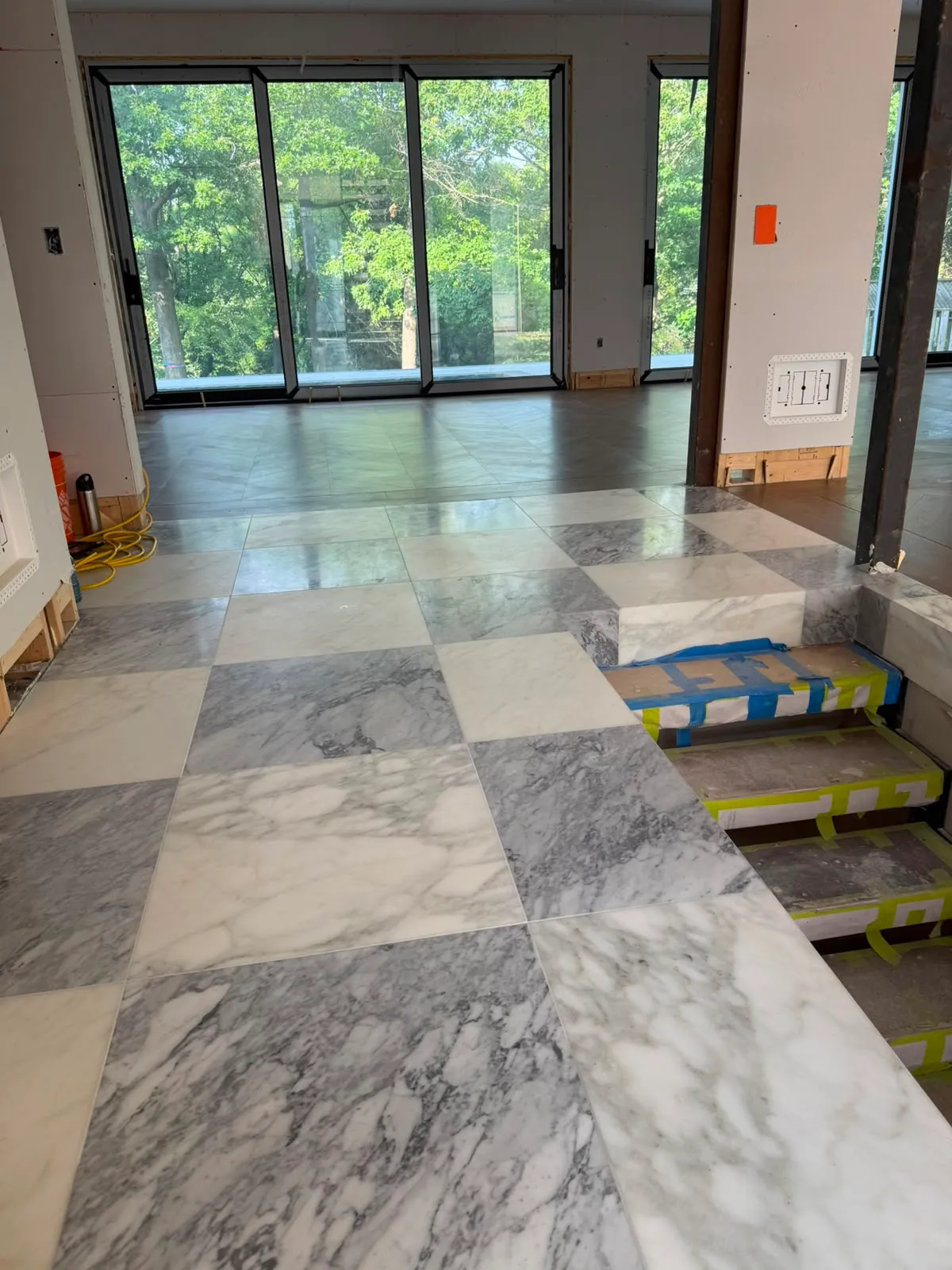 Grey and white marble checkerboard floor with a marble step, the stair treads below wrapped in blue and yellow tape