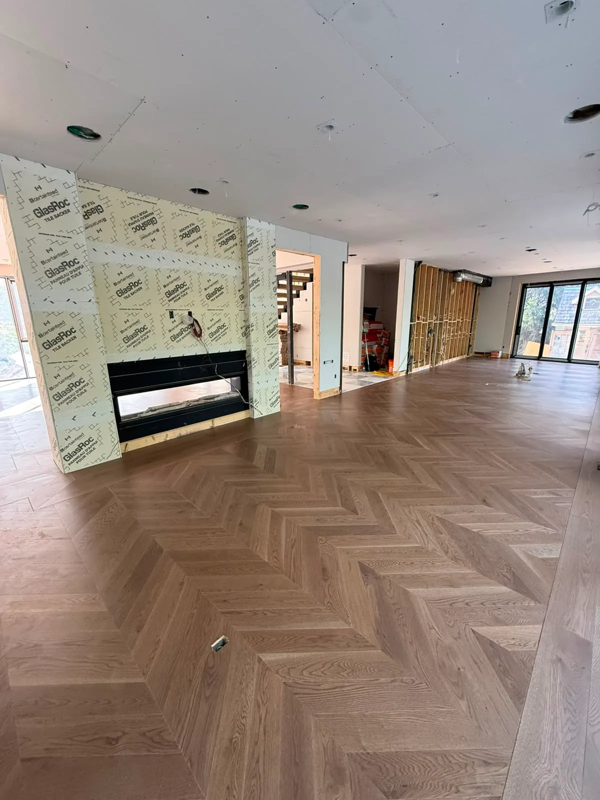 Open main floor with oak herringbone flooring and a linear fireplace set in a wall of tile backer board