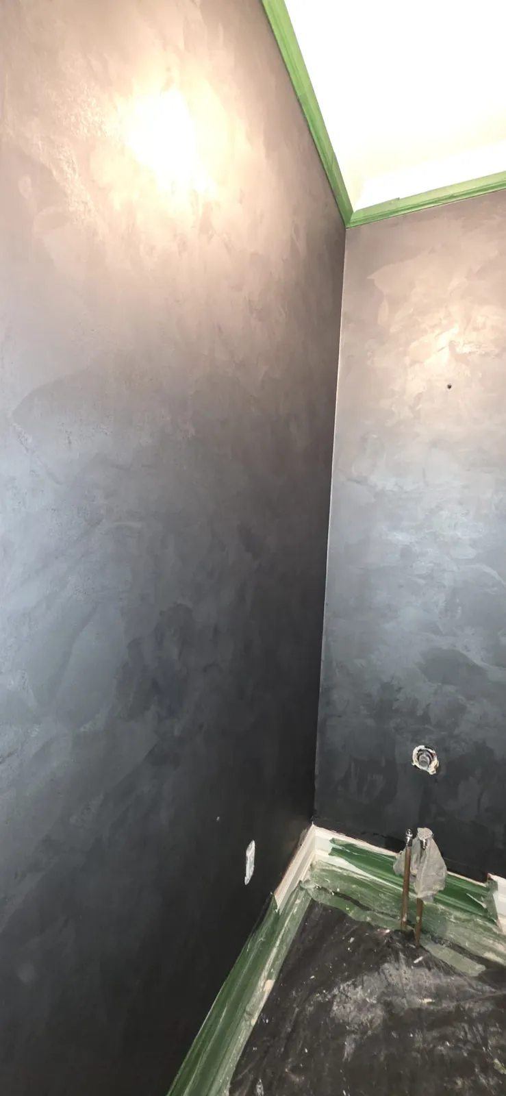 Small washroom with a dark charcoal wall finish, green tape along the ceiling line and baseboard, plastic sheeting on the floor