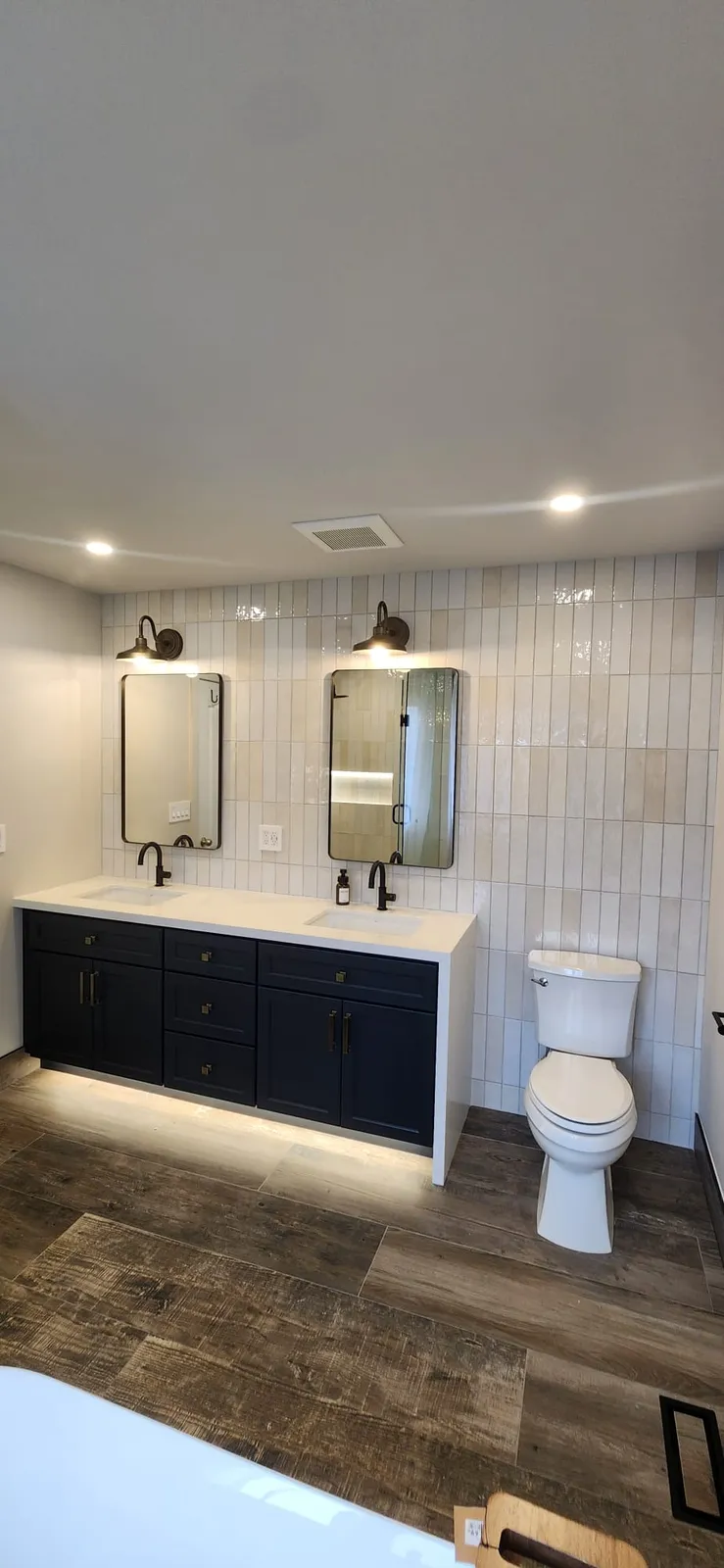 Two black framed mirrors with a wall sconce above each, over a navy vanity with a lit toe kick, beside a toilet