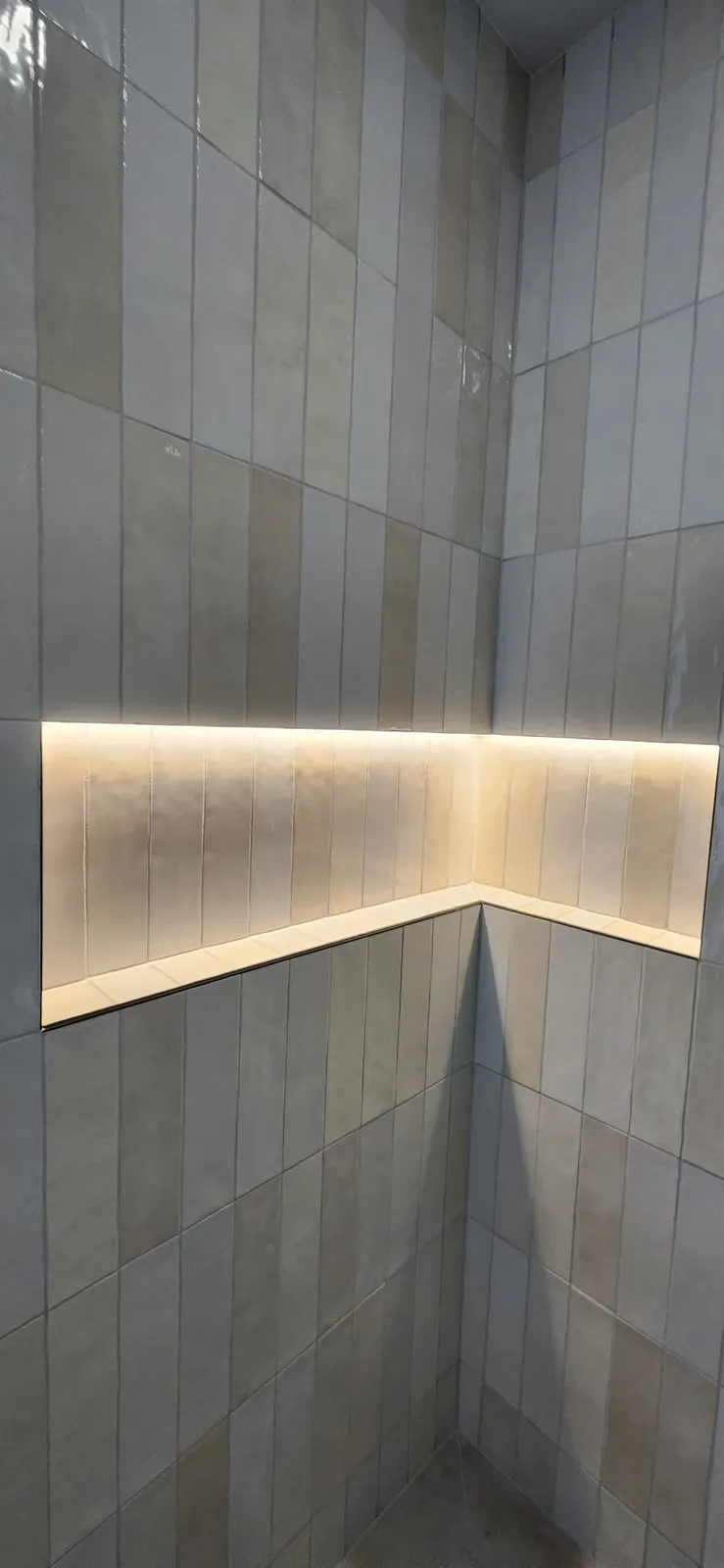 Corner of a shower in white rectangular tile with a long niche lit from inside along both walls