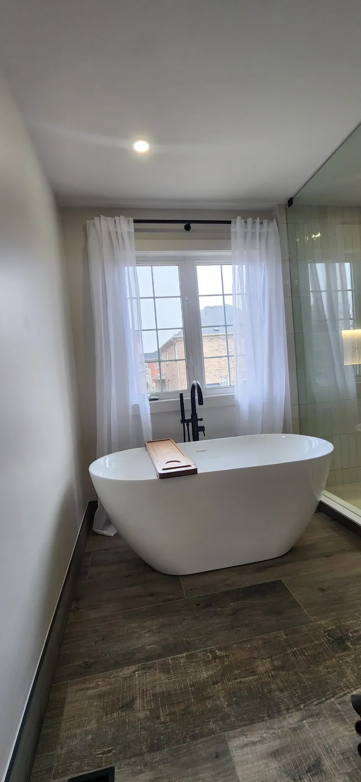 White freestanding tub under a window with sheer curtains, a black floor-mounted faucet beside it