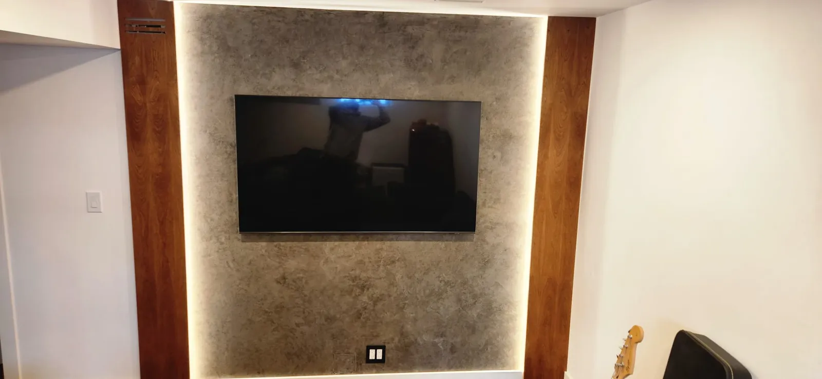TV mounted on a grey plaster wall between two wood posts, with LED light behind the plaster panel