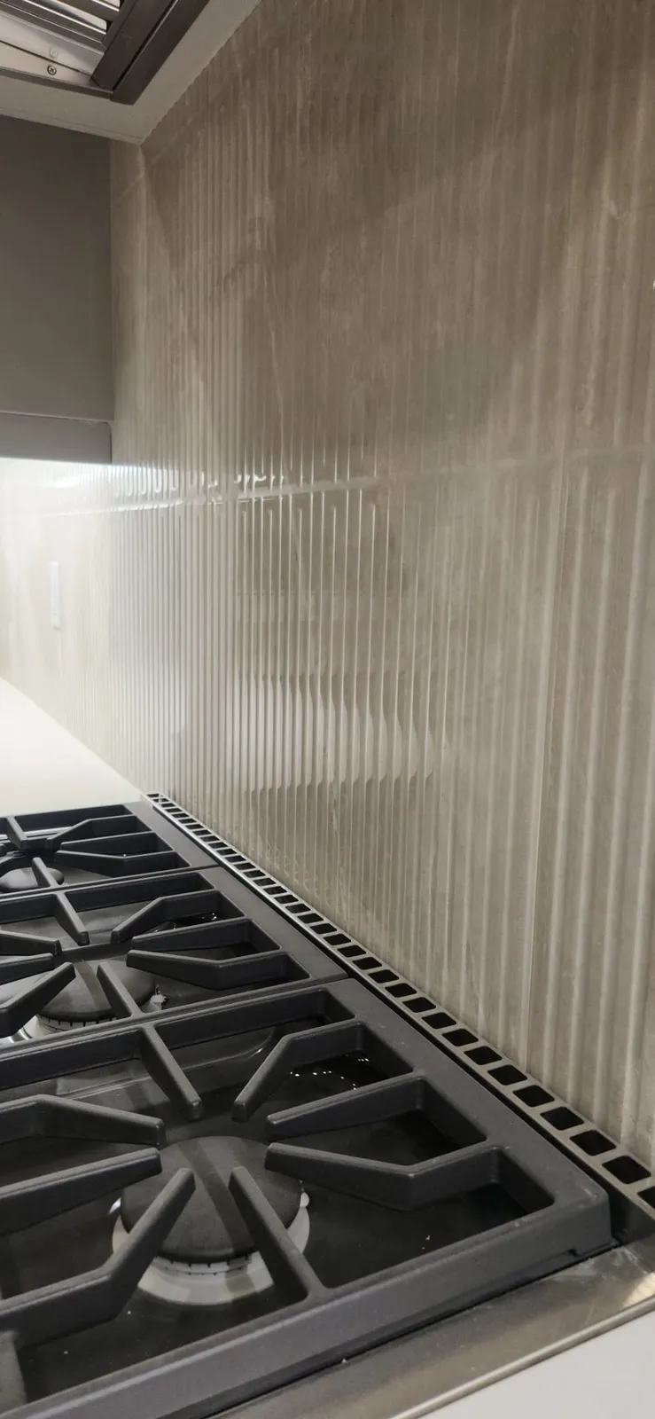 Fluted tile backsplash behind the grates of a gas range, lit by an under-cabinet LED strip