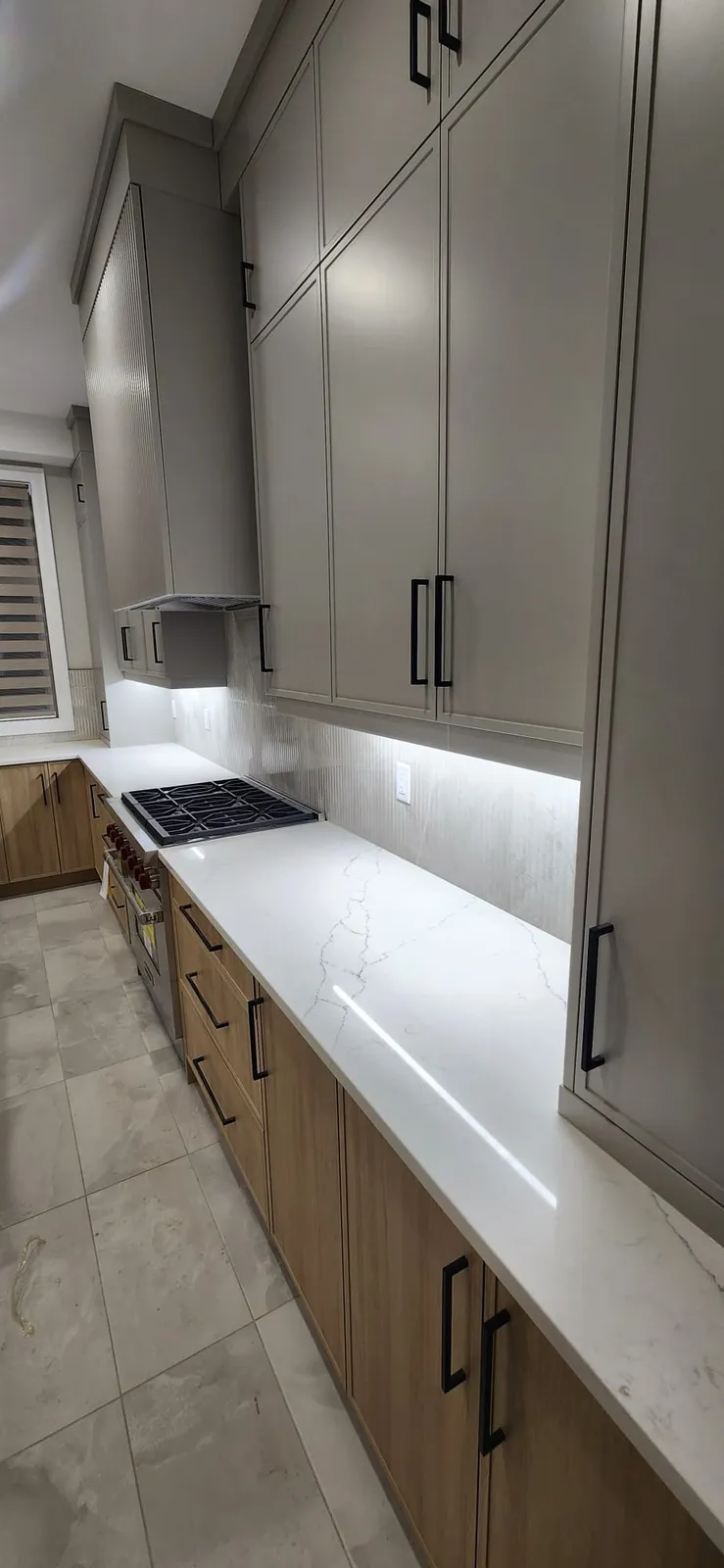 Long counter run with grey upper cabinets to the ceiling over oak-look drawers and large grey floor tiles