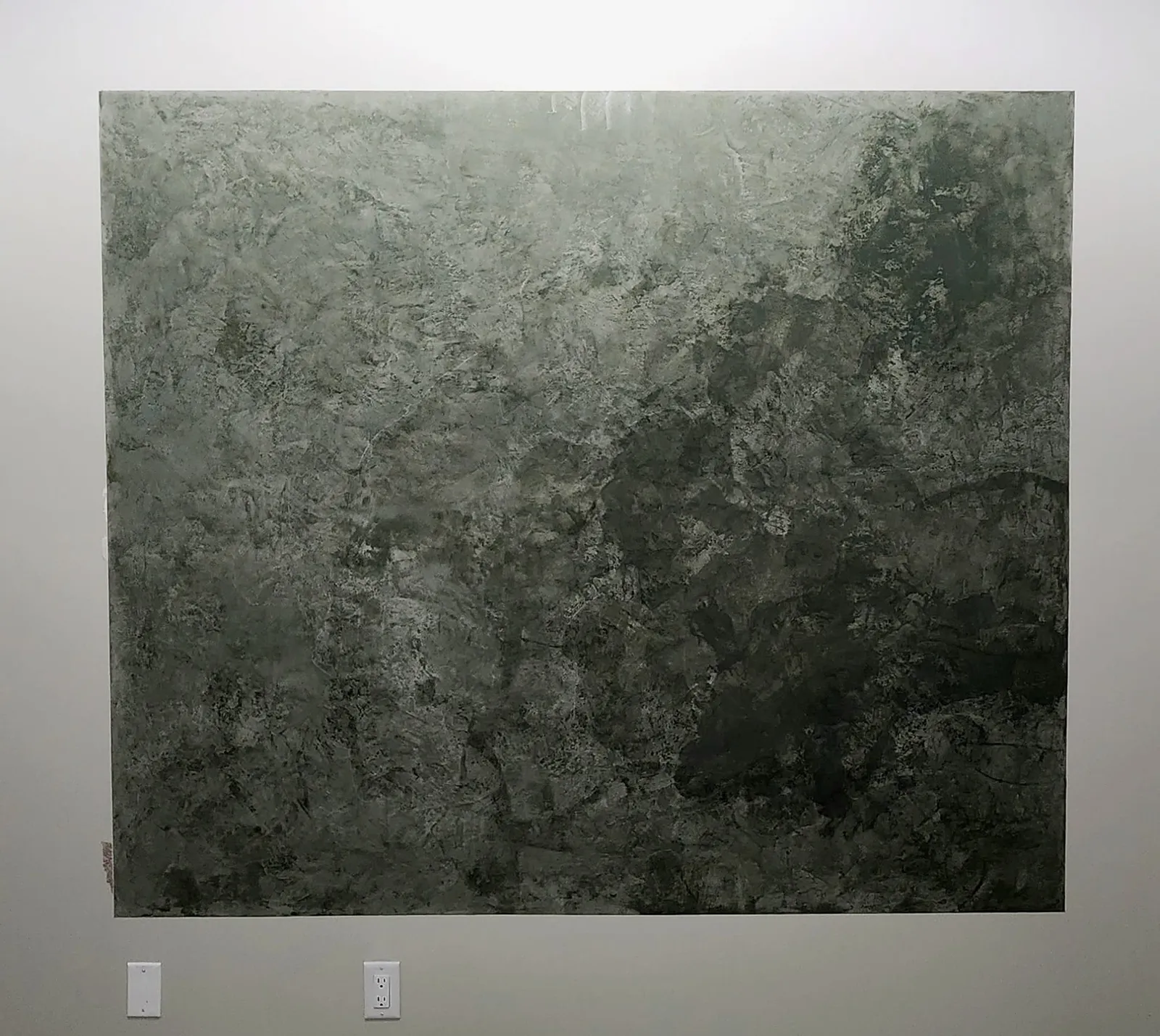 Green decorative plaster panel with dark mottled patches on a light painted wall, a switch plate and an outlet below it