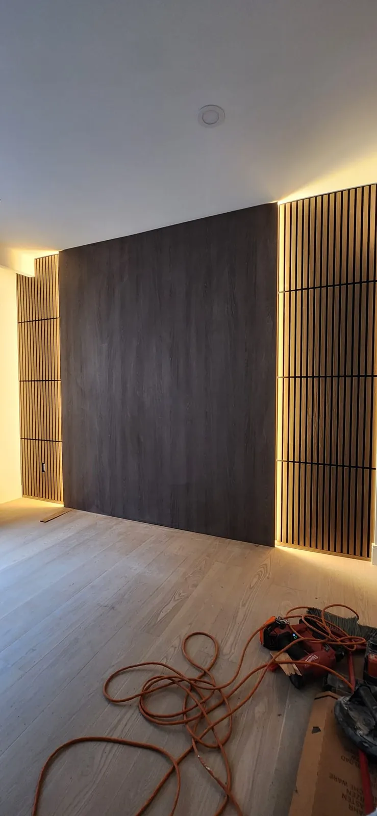 Dark wood-look panel wall flanked by vertical slats with warm LED strips along their edges