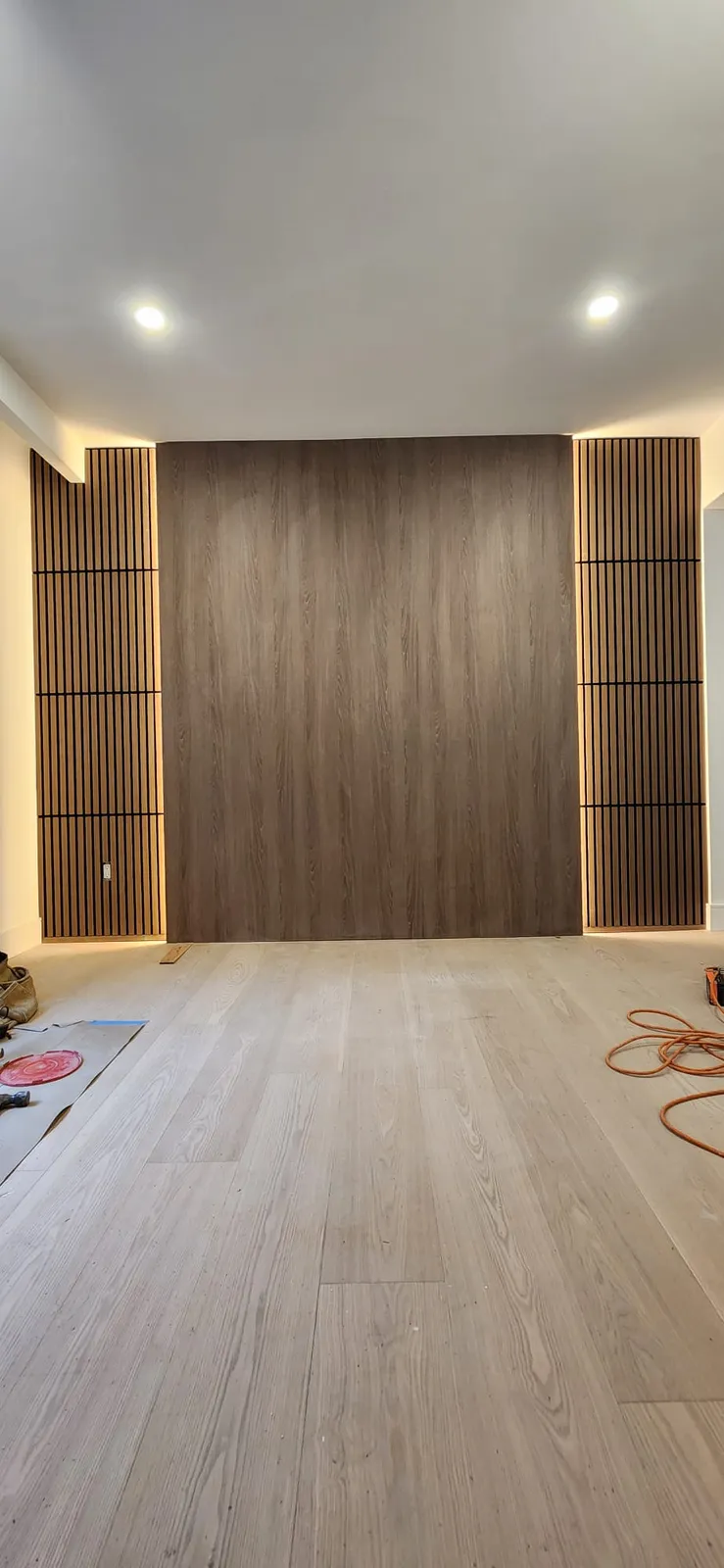 Dark wood panel wall between two lit slat panels above a light wide-plank floor