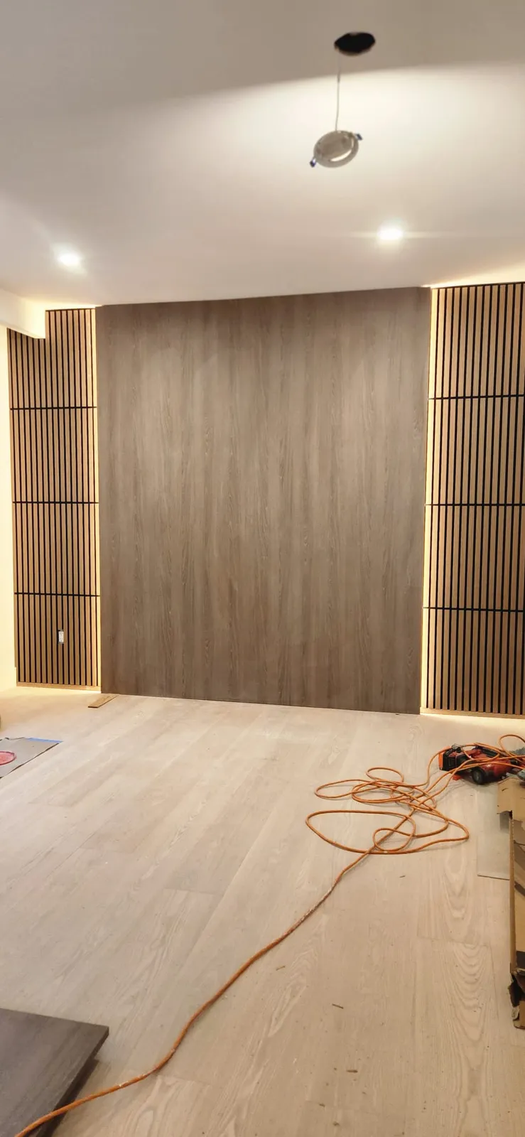 Dark wood-look panel wall between two slatted panels, with an extension cord and tools still on the plank floor